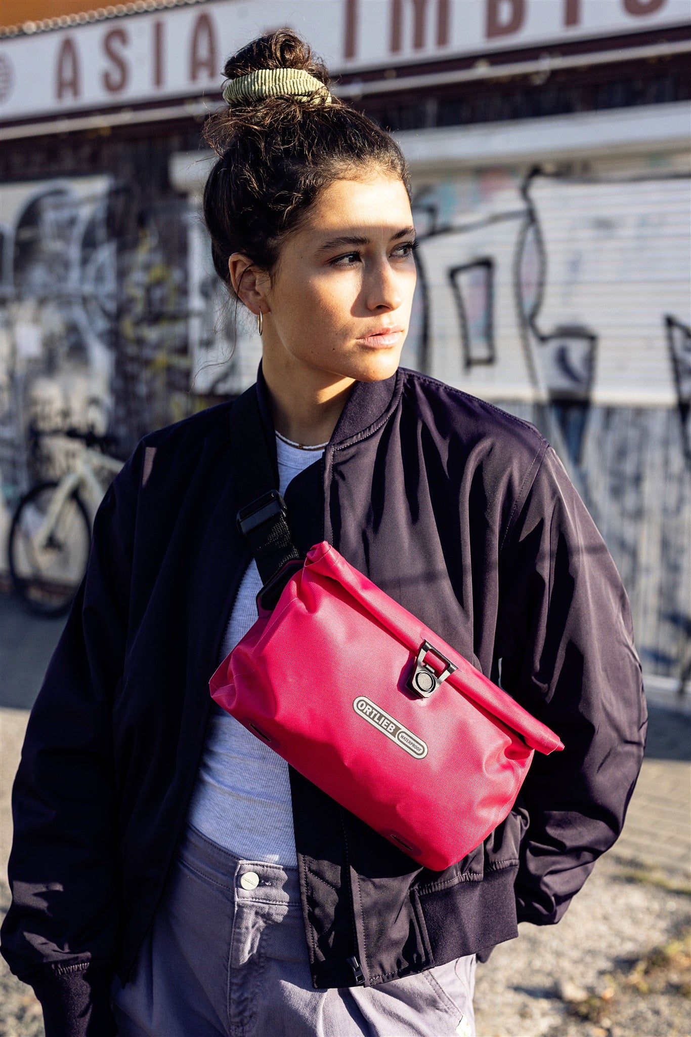 Retrato de mujer con bandolera ORTLIEB Velo-Sling Flex color cyber-pink en entorno urbano.