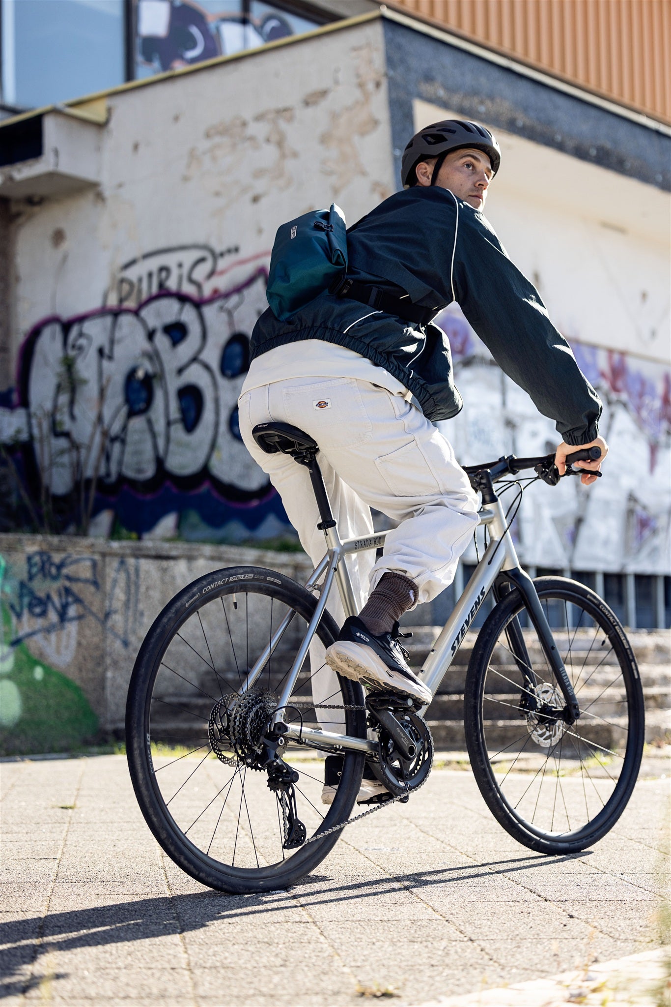 Ciclista con marsupio ORTLIEB Velo-Sling Flex color petrolio in ambiente urbano con graffiti.