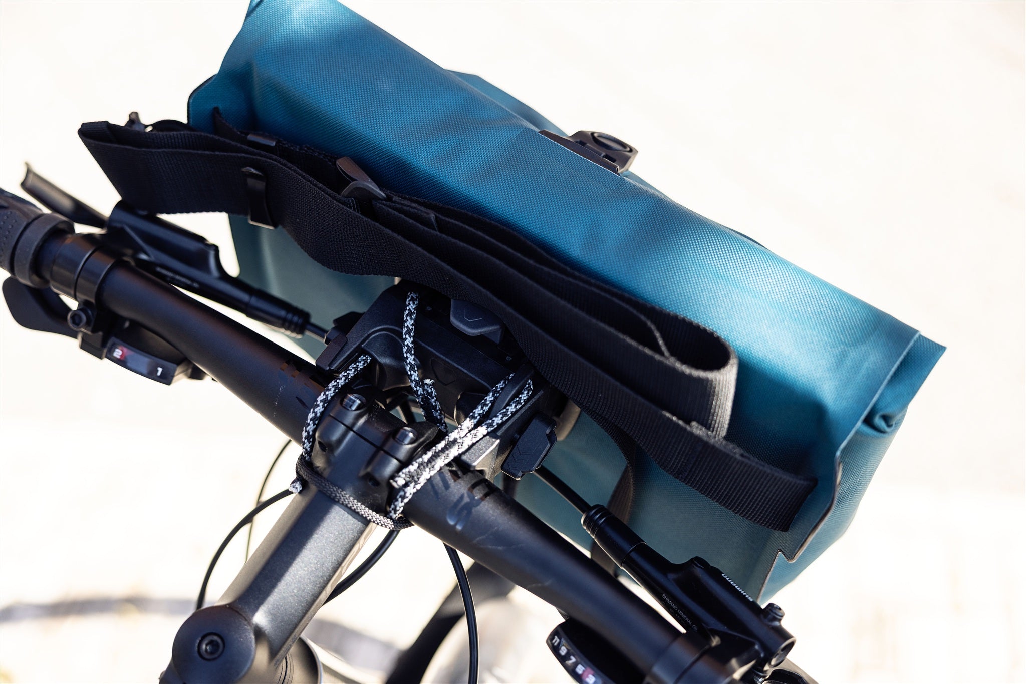 Dettaglio della borsa da manubrio ORTLIEB Velo-Sling Flex color petrolio con supporto Bar-Lock in tessuto impermeabile fissata alla bici.